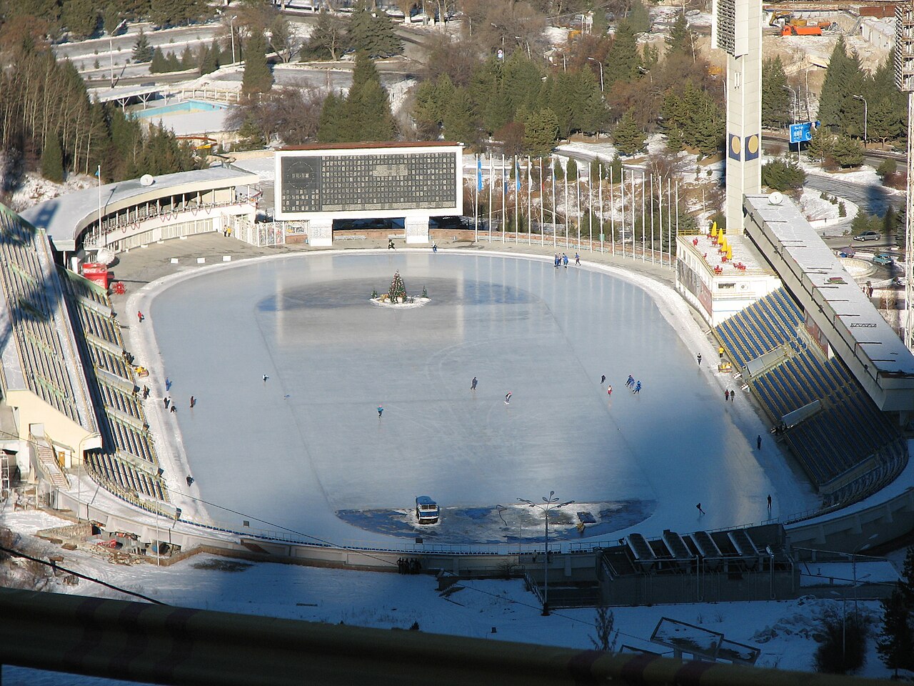 Aerial view of the Medeu high-altitude speed-skating oval above Almaty, skaters on the ice in winter