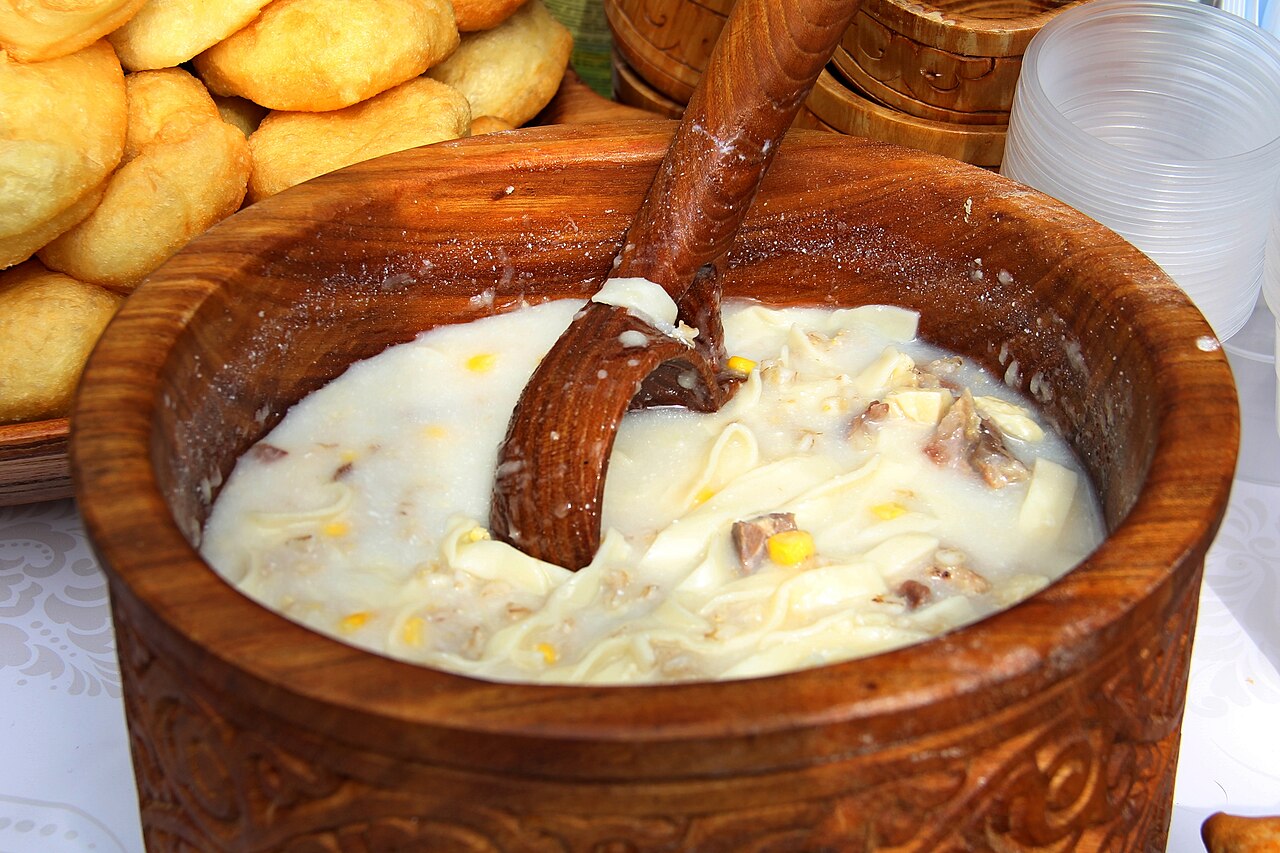 Nauryz kozhe ladled from a carved wooden bowl, with baursak alongside