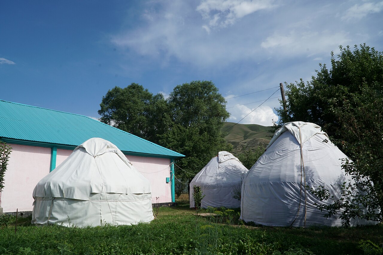 White felt yurts pitched in a guesthouse garden in Saty village below green hills